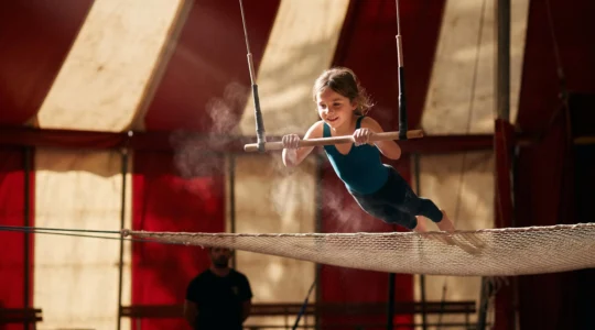 Jeune enfant suspendu a un trapeze dans un chapiteau de cirque francais, symbole de confiance en soi et de motricite