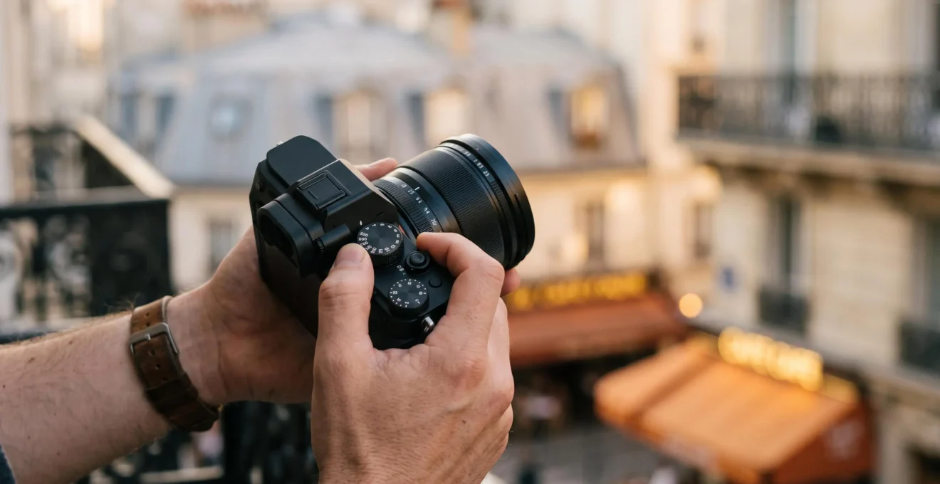 Mains d'un photographe ajustant les commandes manuelles d'un appareil photo dans une rue parisienne au petit matin