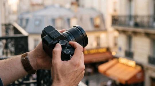 Mains d'un photographe ajustant les commandes manuelles d'un appareil photo dans une rue parisienne au petit matin