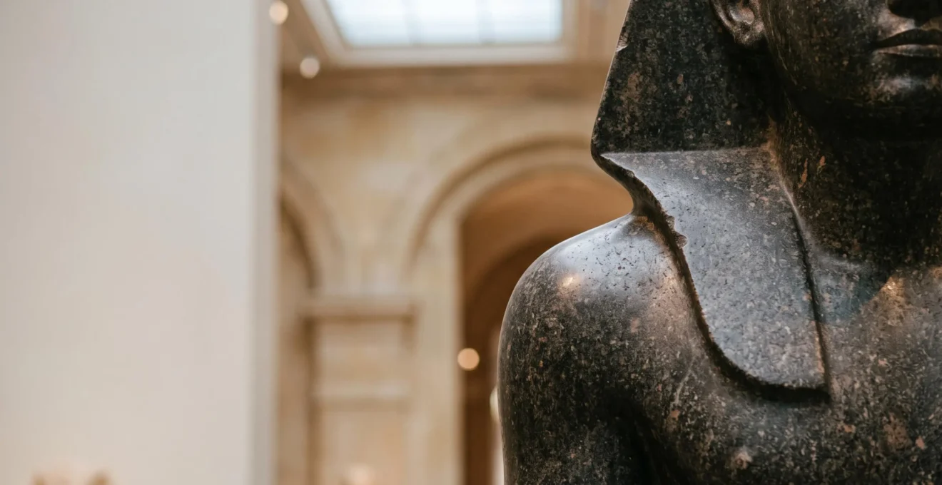 Détail sculpté d'une statue égyptienne en granit exposée dans une galerie de style muséal français, éclairage dramatique soulignant la précision de la taille