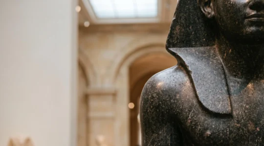 Détail sculpté d'une statue égyptienne en granit exposée dans une galerie de style muséal français, éclairage dramatique soulignant la précision de la taille